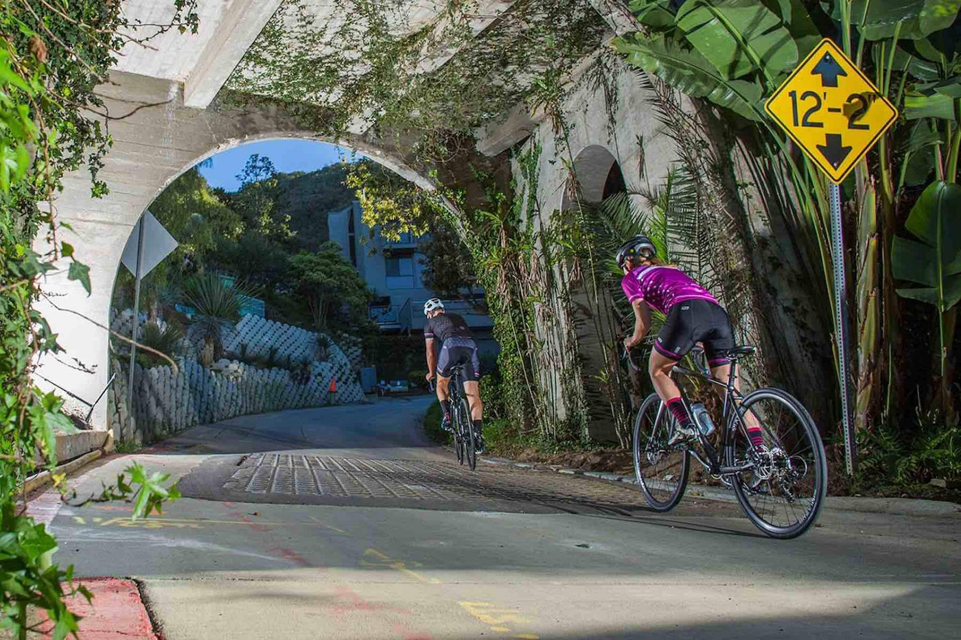 Two road bike riders riding through a bridge under path.
